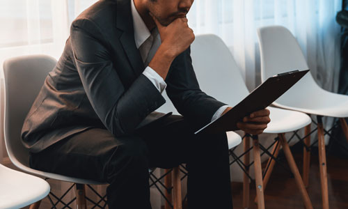  A man sitting in a waiting room holding a clipboard he is studying to prepare for a job interview.