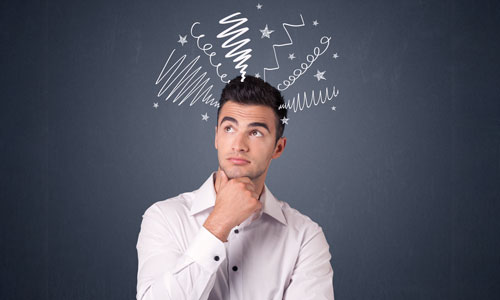 A young man looking puzzled with cartoon chalk scribbles of thoughts coming out of his head. 